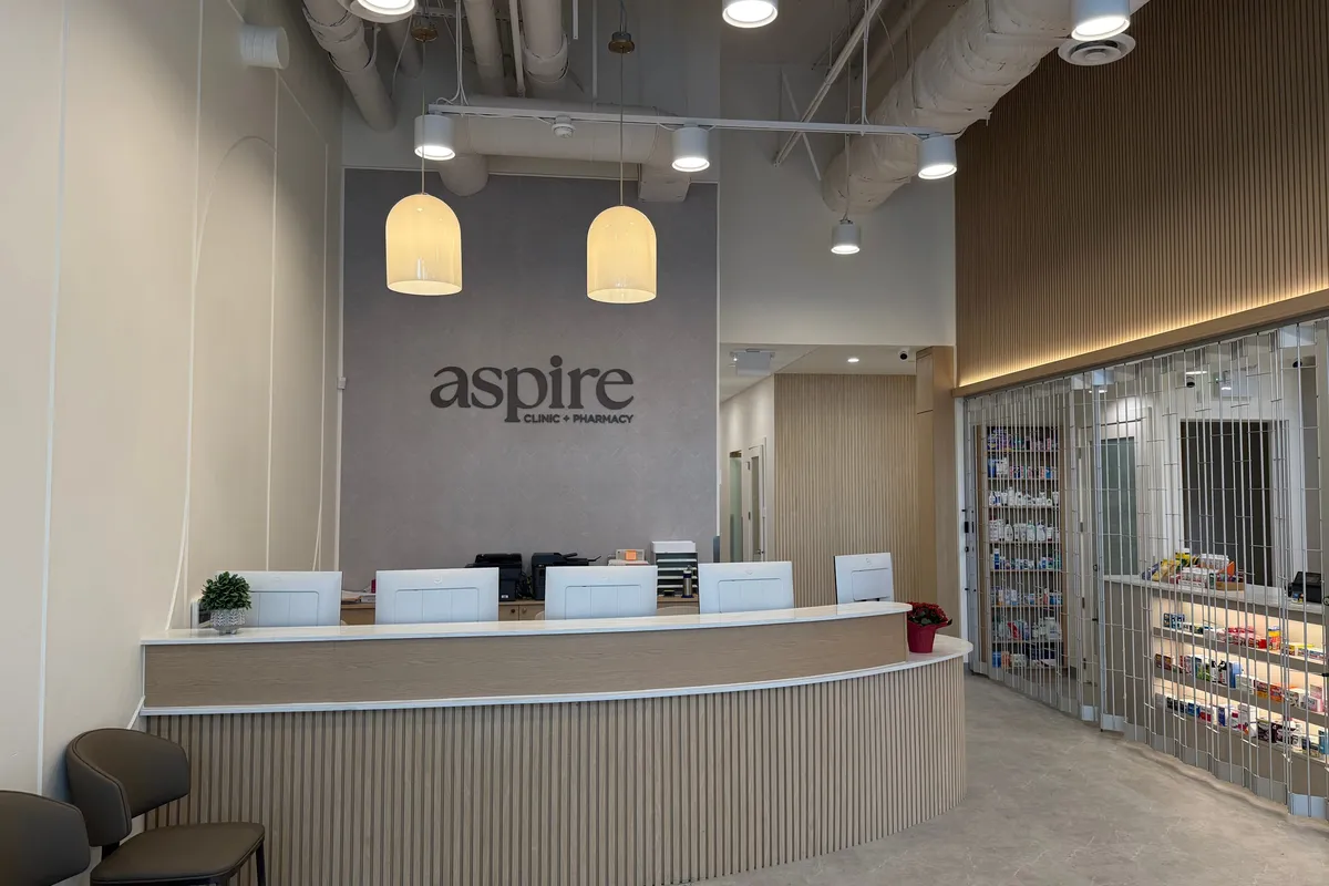 Reception desk detail: curved slatted-oak millwork beneath the aspire Clinic + Pharmacy wall sign