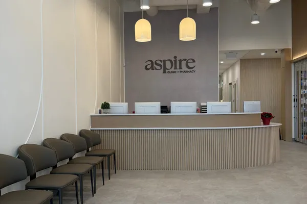 Finished clinic waiting area with a curved slatted-oak reception desk, pendant lighting, and painted exposed services overhead