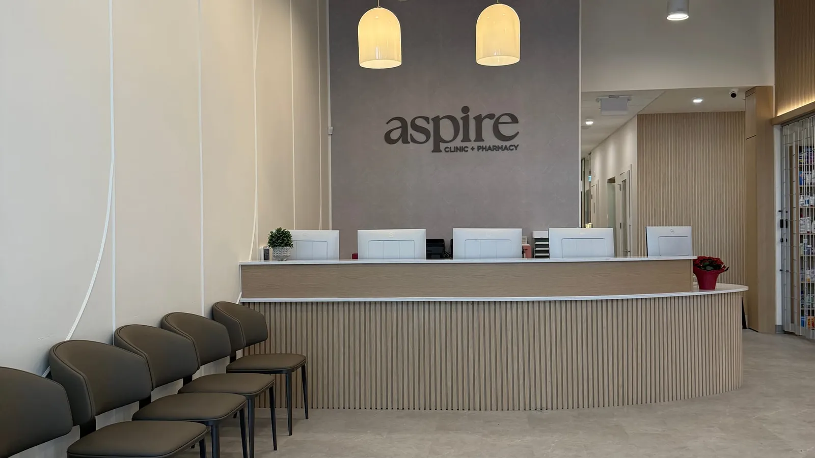 Finished clinic waiting area with a curved slatted-oak reception desk, pendant lighting, and painted exposed services overhead