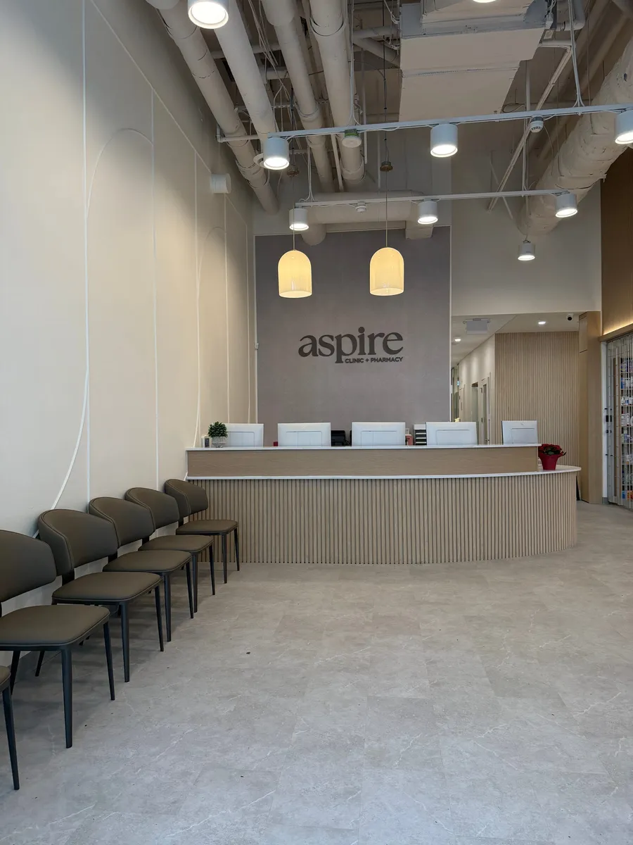Finished clinic waiting area with a curved slatted-oak reception desk, pendant lighting, and painted exposed services overhead