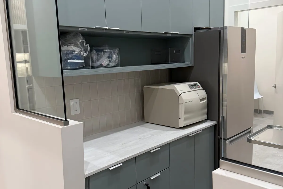 Sterilization bay with grey-green cabinetry, quartz counter, autoclave, and stainless fixtures