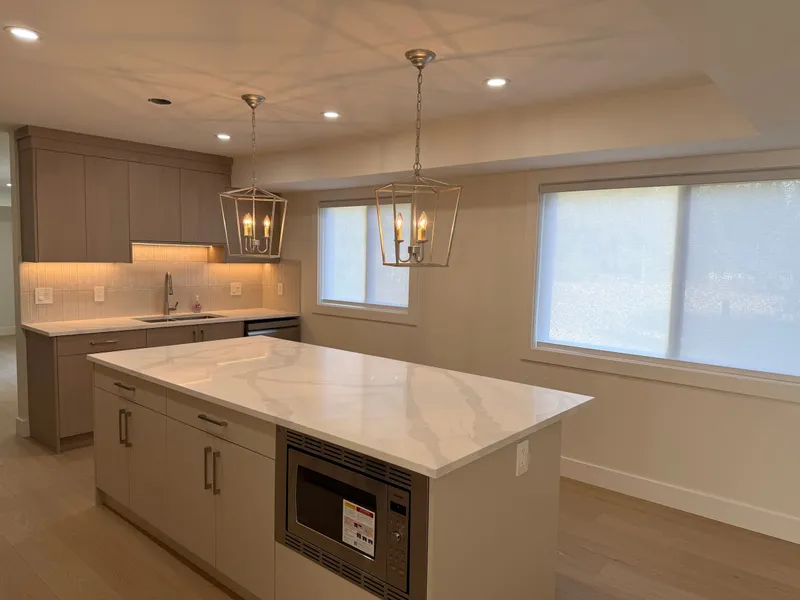 Renovated kitchen with a white quartz waterfall island, taupe shaker cabinetry, and lantern pendants
