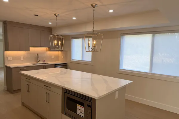 Renovated kitchen with a white quartz waterfall island, taupe shaker cabinetry, and lantern pendant lighting