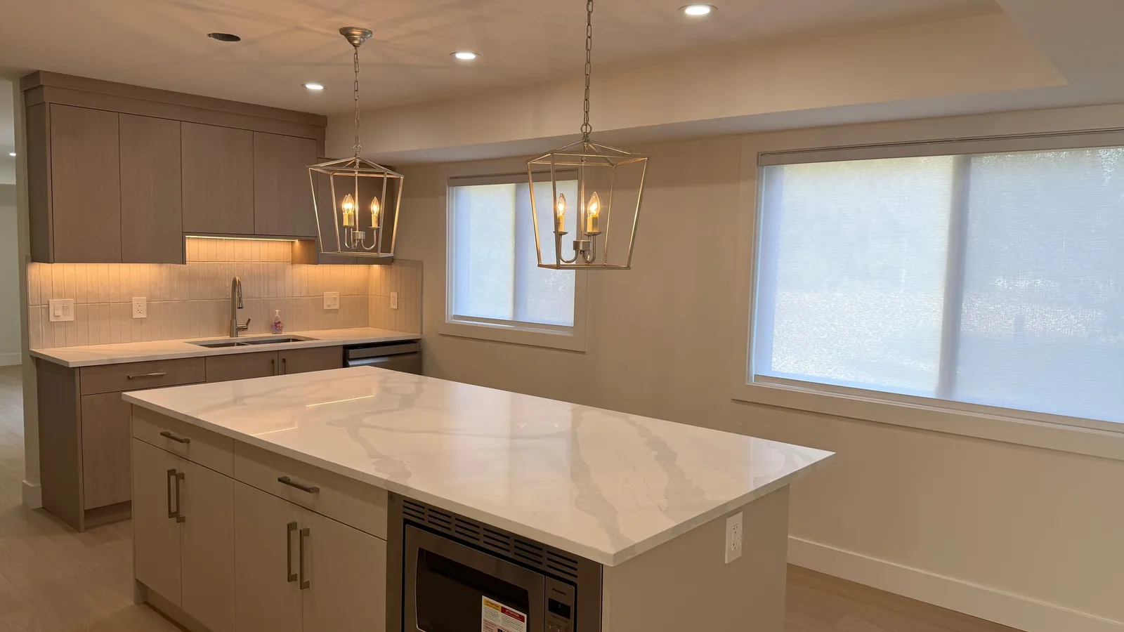 Renovated kitchen with a white quartz waterfall island, taupe shaker cabinetry, and lantern pendant lighting