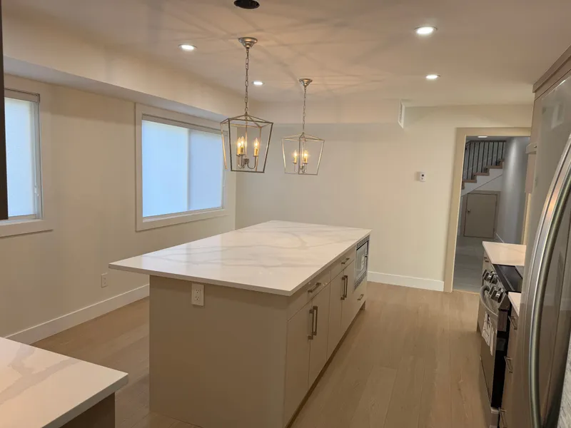 Open-plan kitchen with a quartz island, light wood cabinetry, and stainless appliances