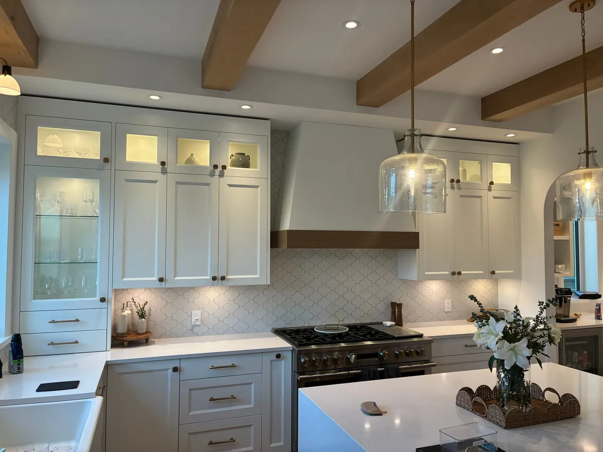 Renovated white shaker kitchen with an arabesque tile backsplash, gas range, and glass-front display cabinets