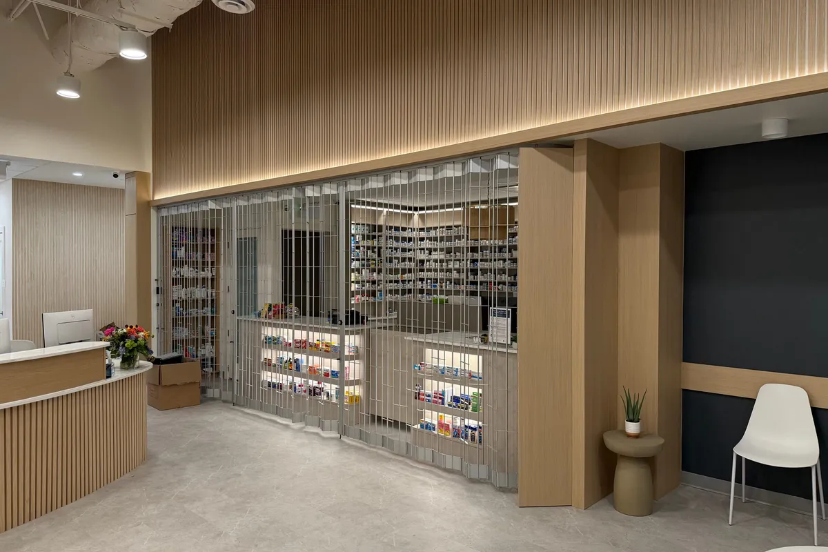 Pharmacy retail floor with backlit product shelving behind a secure roll-down grille