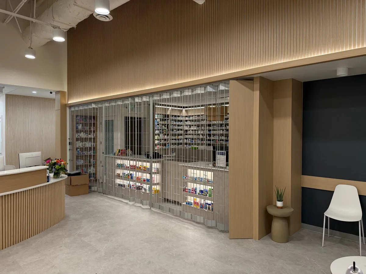Finished pharmacy retail floor with slatted oak walls, backlit shelving, and a secure roll-down grille